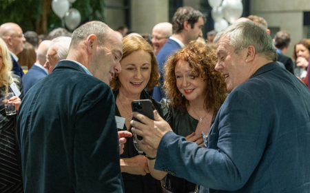 Four alumni at their reunion, looking at a phone screen and smiling.